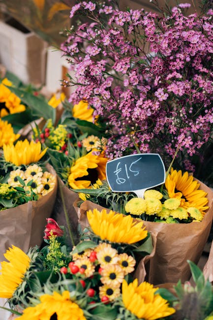 A vibrant display of fresh floral arrangements outdoors, featuring bouquets wrapped in brown paper, predominantly composed of bright yellow sunflowers and smaller cheerful daisies with white petals an
