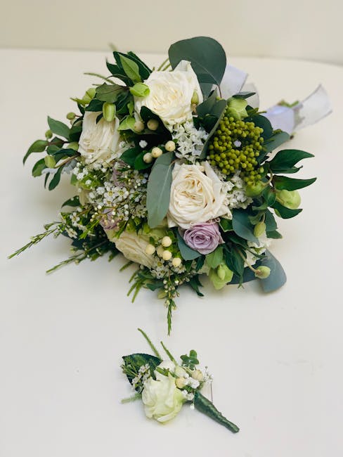 A bouquet of fresh wedding flowers arranged with white roses, pale purple lisianthus, and small white filler flowers, accented by green foliage including eucalyptus leaves. The bouquet is neatly tied 
