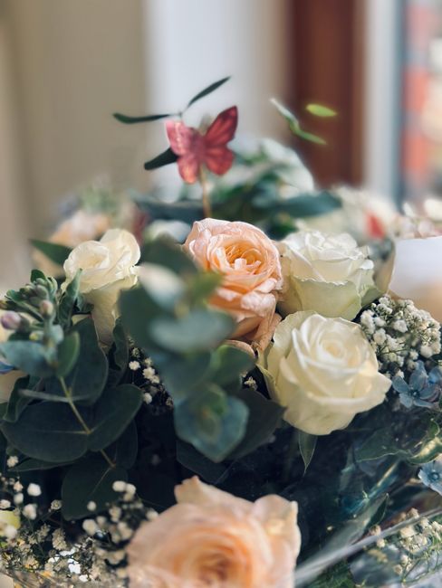 A floral arrangement featuring a mix of fresh roses in soft cream and blush pink tones, complemented by sprigs of baby's breath and eucalyptus leaves. The bouquet is artistically arranged with the ros